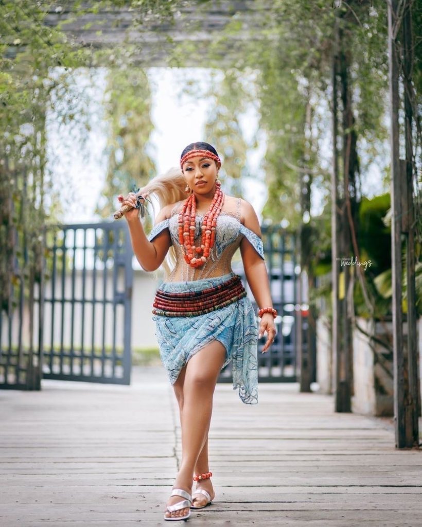 A colorful photo of Rita Dominic wearing a traditional Igbo bridal attire, including coral beads and a headpiece.